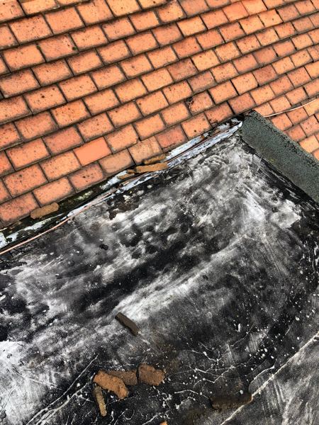 Old coated flat roof lifting away where it meets the tiled slope