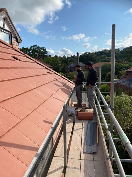 Roofers working from the scaffold beside the new red tiles and dormer