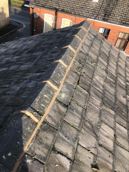 Slate roof ridge with fresh mortar along the joints and edges, terraced street beyond