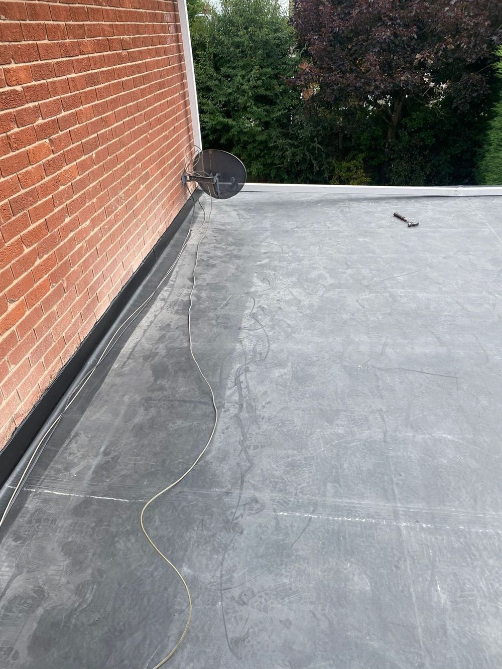 The same roof finished, the covering taken up the brick house wall as an upstand and run out to the white fascia along the far edge