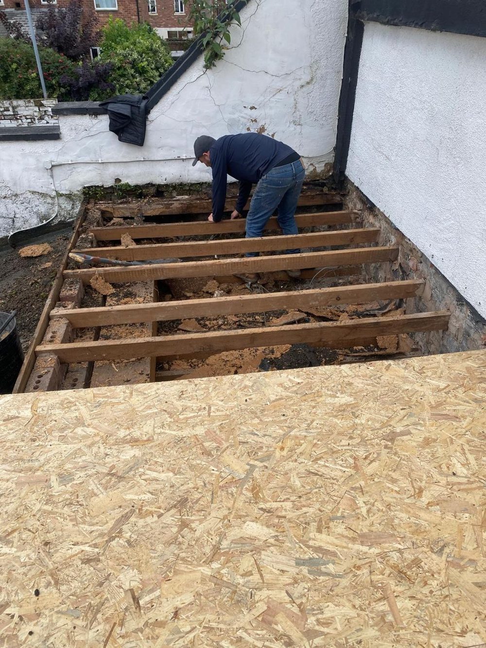 A flat roof stripped back to bare joists, with the first sheets of the new deck already down alongside