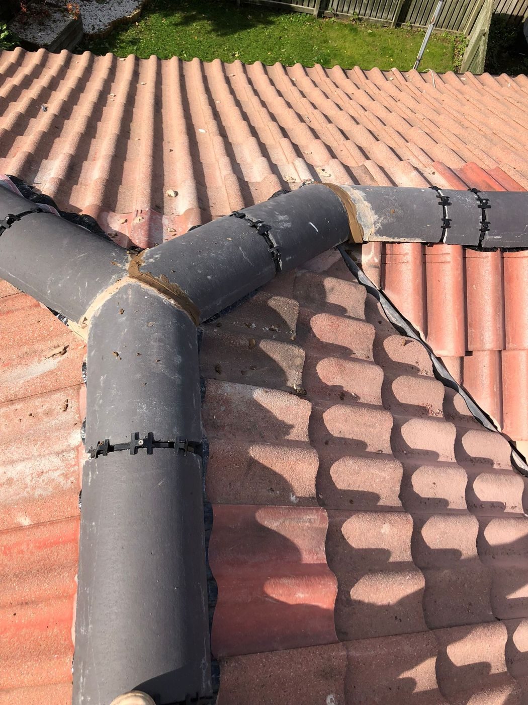 Grey ridge and hip tiles meeting at a junction, clipped down and pointed, above red interlocking tiles